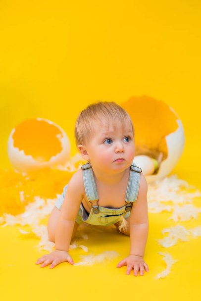 baby sits with decorative Easter eggs on a yellow background. the concept of Easter - Photo, Image