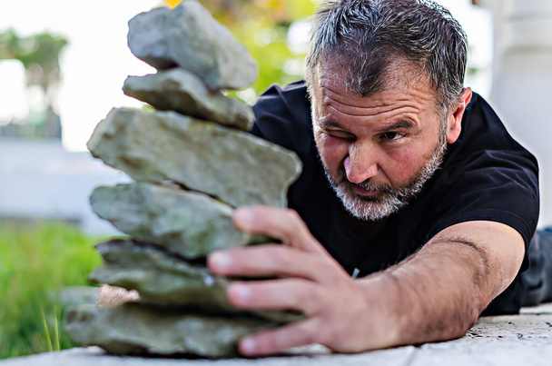 Άντρας συγκεντρωμένος με το ένα μάτι κλειστό σε πέτρες στερέωσης σε ισορροπία - Φωτογραφία, εικόνα