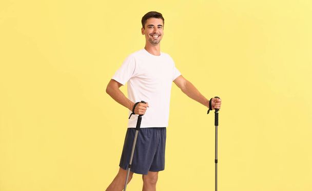 Hombre joven con bastones para caminar sobre fondo de color - Foto, imagen