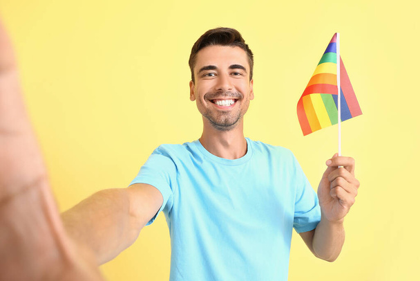 Jeune homme avec drapeau LGBT prenant selfie sur fond de couleur - Photo, image