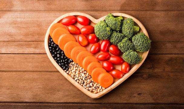 Top view of fresh organic fruits and vegetables in heart plate wood (carrot, Broccoli, tomato) on wooden table, Healthy lifestyle diet food concept - Foto, Imagem