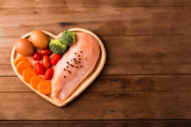 Top view of Raw chicken breasts fillets no boneless with spices rosemary, carrot, and eggs in heart plate wood on wooden background, Healthy food day concept - Fotó, kép
