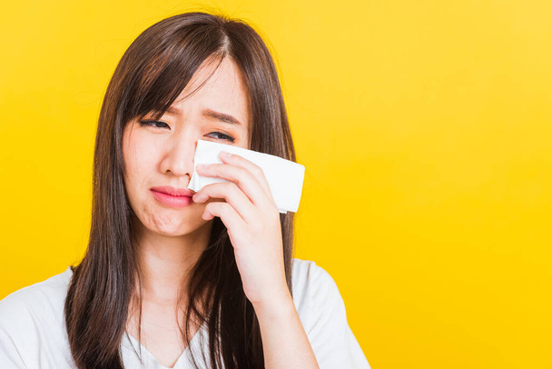 Portrait of Asian beautiful young woman sad she crying wiping tears from eyes with a tissue, Close up of pretty girl feeling depressed upset unhappy, studio shot isolated on yellow background - Foto, afbeelding