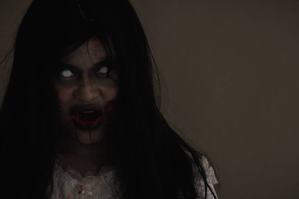 Girl zombie in blood. Closeup face and eyes of Asian Woman ghost with blood. Horror creepy scary fear in a dark house. Hair covering the face, Halloween festival concept - Foto, Imagen