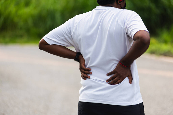 Close up Asian young sport runner black man wear watch feel pain on his spine low back and hip while running at the outdoor street health park, healthy exercise Injury from workout concept - 写真・画像