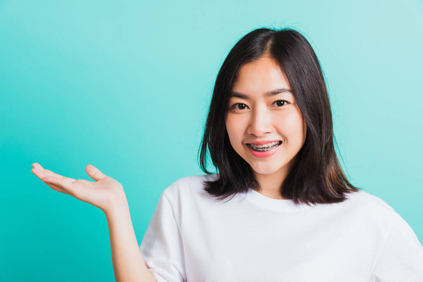 Portrait of Asian teen beautiful young woman smile have dental braces on teeth laughing she show hand side blank space, isolated on a blue background, Medicine and dentistry concept - Zdjęcie, obraz