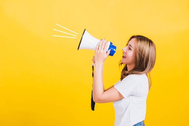 Asian Thai happy portrait beautiful cute young woman stand to make announcement message shouting screaming in megaphone looking to side away, studio shot isolated on yellow background with copy space - Φωτογραφία, εικόνα
