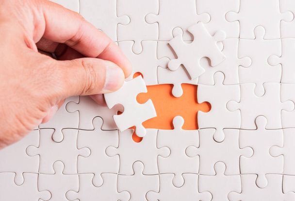 Top view flat lay of hand-holding last piece white paper jigsaw puzzle game last pieces put to place for solve problem complete mission, studio shot on an orange background, quiz calculation concept - Photo, image