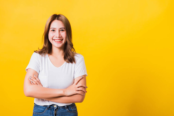 Asian Thai happy portrait beautiful cute young woman standing wear t-shirt her smile confidence with crossed arms looking to side up isolated, studio shot on yellow background and copy space - Photo, image