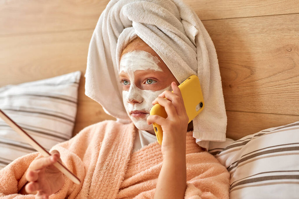 attractive kid girl talk on phone lying on bed - Fotografie, Obrázek