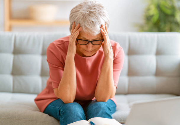 Erschöpfte Seniorin mit Kopfschmerzen sitzt zu Hause auf Sofa.  - Foto, Bild