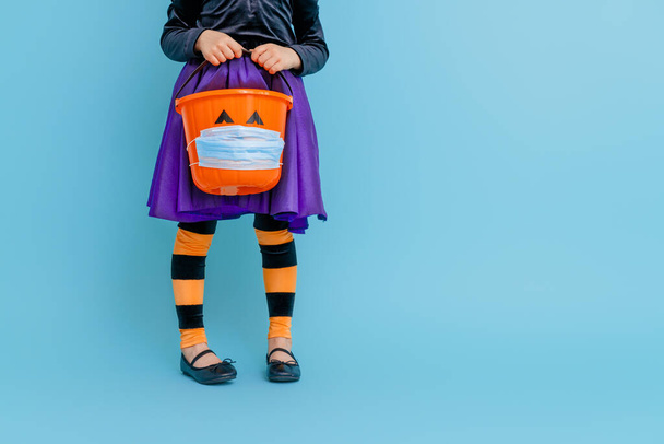 Happy Halloween! Little kid with a basket for sweets  wearing face mask protecting from COVID-19. - Foto, immagini
