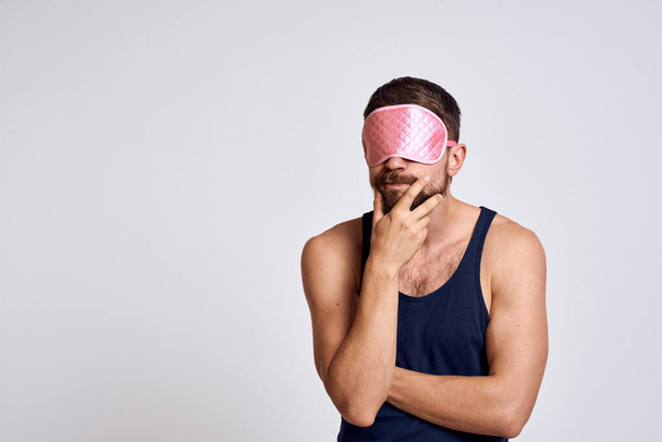 Un hombre con una máscara de sueño rosa Y una camiseta negra sobre un fondo gris recortado vista - Foto, imagen