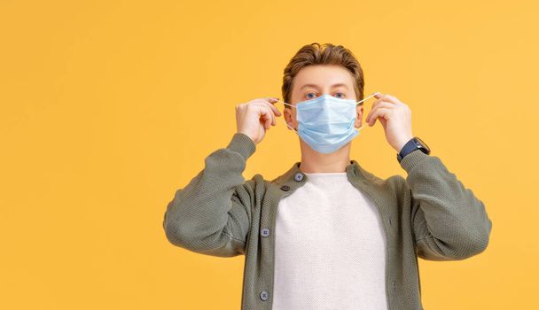 Young man wearing facemask during coronavirus and flu outbreak. Virus and illness protection, home quarantine. COVID-2019. Taking on or taking off masks. Person on yellow color background. - Foto, Bild