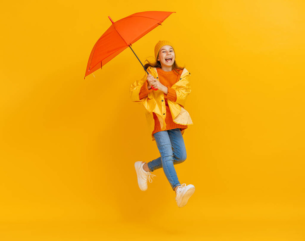 Happy emotional child laughing and jumping. Kid with orange umbrella on colored red background. - Zdjęcie, obraz