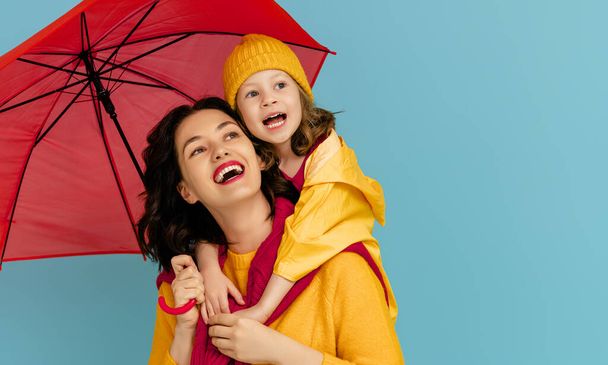 Happy emotional child and mother laughing and hugging. Family with red umbrella on colored teal background. - Foto, imagen