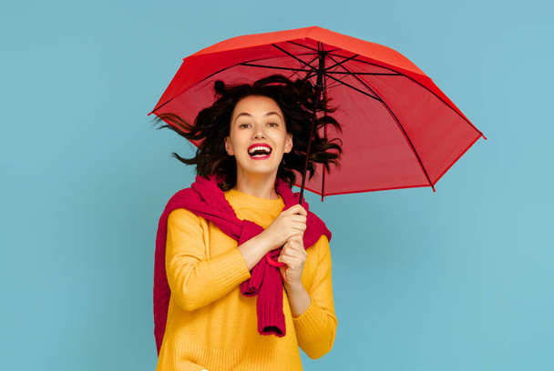Happy emotional young woman laughing with red umbrella on color teal background. - Foto, Imagen