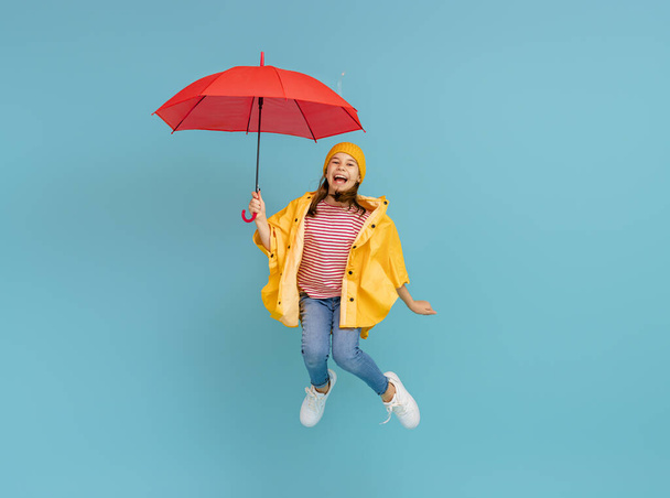 Happy emotional child laughing and jumping. Kid with red umbrella on colored teal background. - Fotoğraf, Görsel