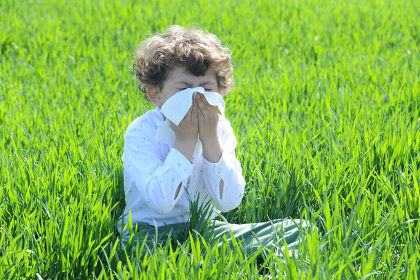 Kleine Europese blanke kinderen heeft allergieën van bloem stuifmeel, jongen heeft lopen neus in bloemenveld en veeg zijn neus door tissuepapier - Foto, afbeelding