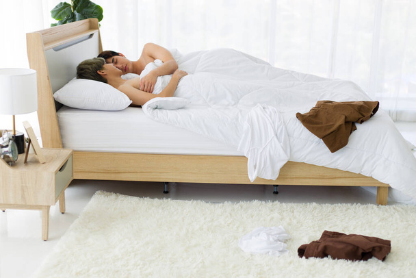 Onnelliset aasialaiset homoseksuaaliset miehet tai homoparit makaavat valkoisella sängyllä, molemmat syleilevät yhdessä rakkauden tuulella, kun heidän vaatteensa ovat lattialla. HLBTQ-ylpeyden käsite. - Valokuva, kuva