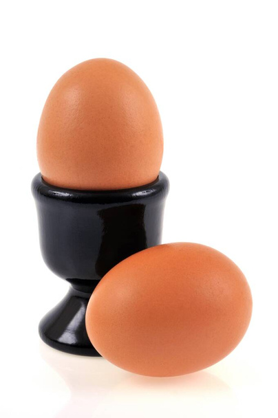 Черный стакан яйца и свежие яйца крупным планом на белом фоне  - Фото, изображение