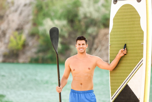 Young man with board and paddle for sup surfing near river - Fotoğraf, Görsel