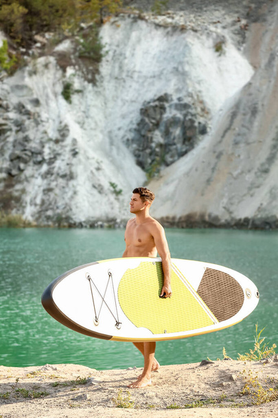 Jongeman met board voor sup surfen in de buurt van rivier - Foto, afbeelding
