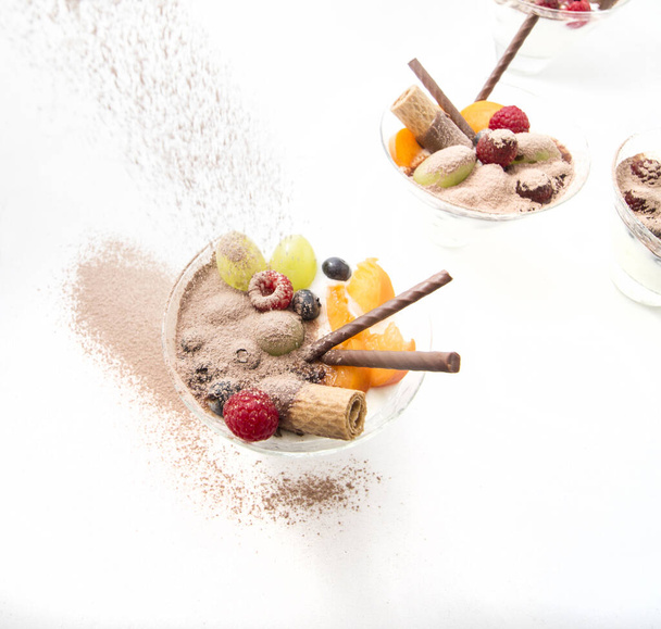 fruit met yoghurt in kristallen glazen versierd met chocolade koekjes en cacaopoeder. Gezond ontbijt. - Foto, afbeelding