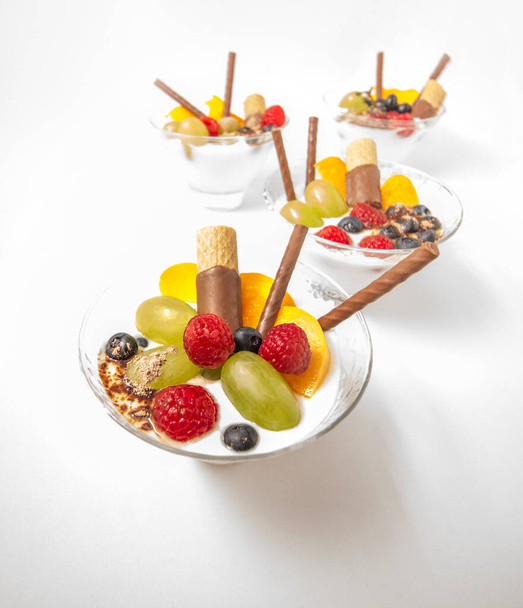 fruit met yoghurt in kristallen glazen versierd met chocolade koekjes en cacaopoeder. Gezond ontbijt. - Foto, afbeelding