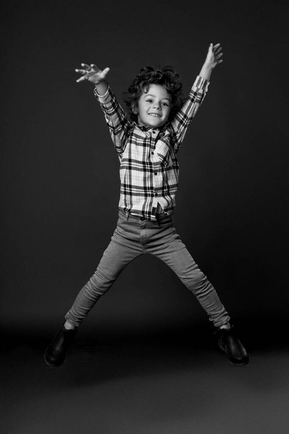Frontalny portret skaczącego chłopca z rękami i nogami, pokazuje jego radość, koncepcję szczęśliwego dziecka, wolność. Czarno-biały obraz. izolowany na czarnym tle. - Zdjęcie, obraz