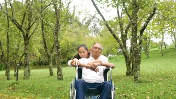Щасливий усміхнений дідусь у інвалідному кріслі розслабляється і гуляє з онукою на відкритому повітрі в парку. Сімейний щасливий спосіб життя
. - Кадри, відео