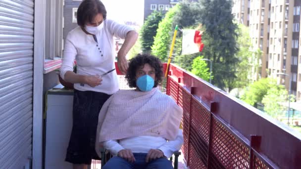 Europa, Itália, Milão - Emergência pandémica n-cov19 Coronavirus - Vida doméstica em quarentena de 70 anos Senhora idosa italiana com máscara cortar o cabelo na varanda de casa para filho - Filmagem, Vídeo