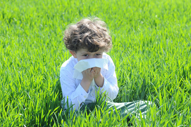 Маленькі європейські діти - каказіати мають алергію на пилок квітів, хлопчик має ніс у квітковому полі і витирає ніс тканиною паперу. - Фото, зображення