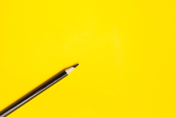 diagonal black sharp wooden pencil on a bright yellow background, isolated, copy space, mock up - Foto, afbeelding