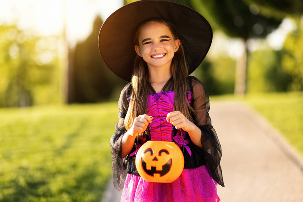 heureuse fille enfant dans un costume de carnaval et avec un seau de citrouille le jour d'Halloween en plein air - Photo, image
