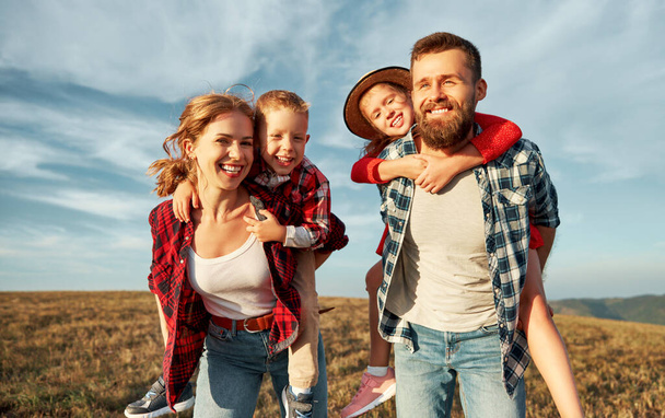 Glückliche Familie: Mutter, Vater, Kinder Sohn und Tochter umarmen sich, lachen und haben Spaß auf dem Gras, lachen und spielen in der Natur vor blauem Himmel - Foto, Bild