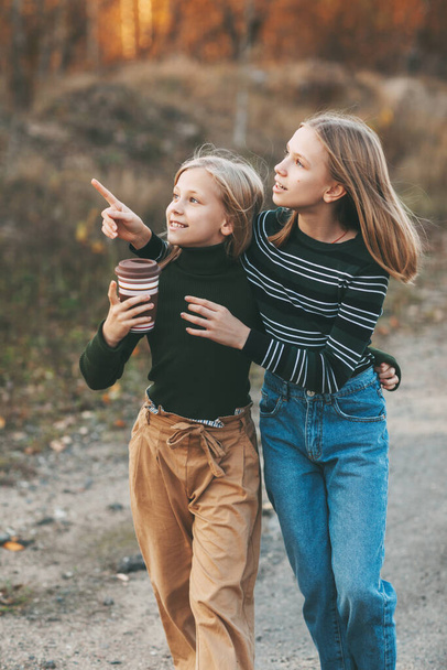 De twee zussen keren terug van school en praten terwijl ze door een openlucht herfstpark rijden. - Foto, afbeelding