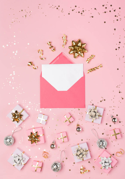 Christmas composition. Gold and silver decorations, mirror disco balls, gifts, envelope, card on pastel pink paper background. Christmas, winter, new year concept. Flat lay, top view, copy space. - Foto, Bild