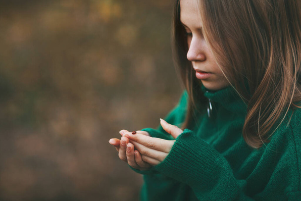 Hermosa adolescente rubia en un suéter verde cálido con una mariquita en un parque de otoño. Primer plano - Foto, imagen