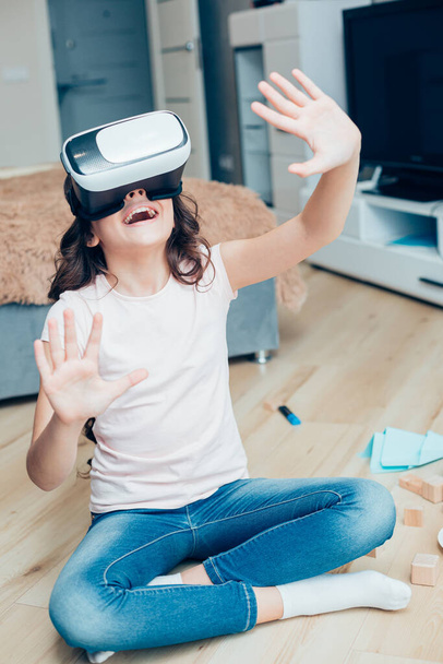 Positives Mädchen mit moderner Virtual-Reality-Brille auf dem Boden ihres Schlafzimmers - Foto, Bild
