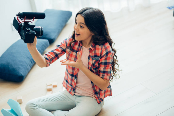Expressive pretty girl sitting on the floor and gesturing while talking on a camera and recording herself - Photo, image