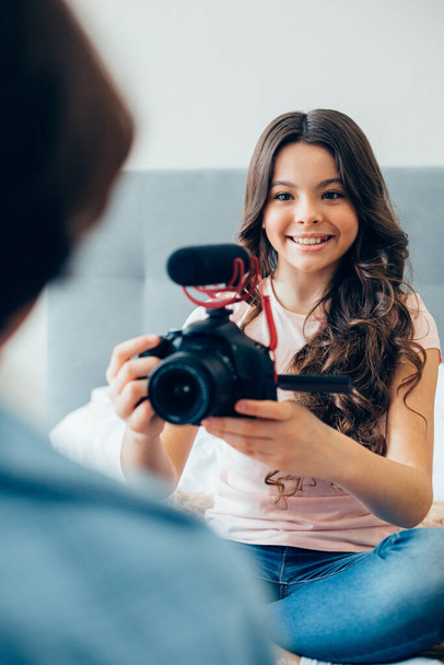 Beautiful girl smiling and using a modern camera with a microphone adjusted to it while recording some content for her blog - 写真・画像
