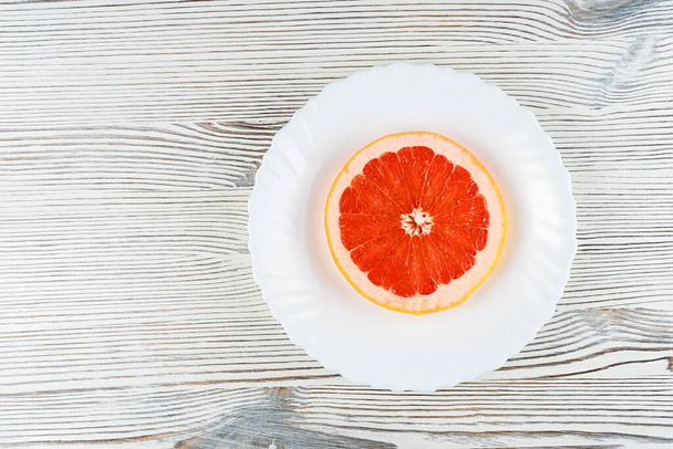 A fresh grapefruit on a white plate on a wooden background - Foto, Bild