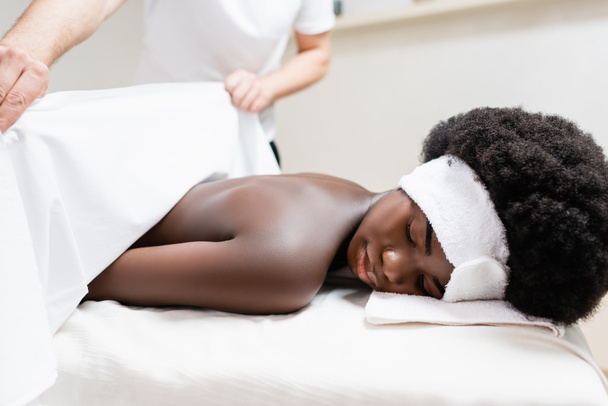 Masseur couvrant femme afro-américaine avec drap de lit dans le salon de spa, bannière - Photo, image