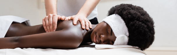 Massaggiatore massaggiando donna afro-americana indossando fascia bianca nel salone spa, banner - Foto, immagini