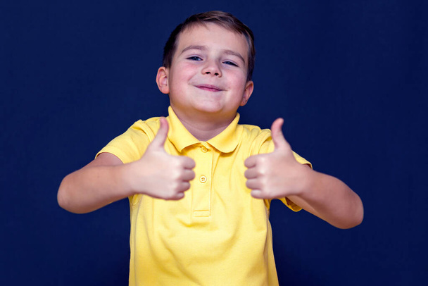 Bello giovane ragazzo 9s mostra una classe con due pollici su su uno sfondo blu. - Foto, immagini