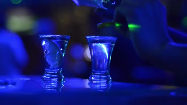 vista parcial de vídeo de la persona con tazas de tequila en el bar con luces azules del club nocturno  - Imágenes, Vídeo