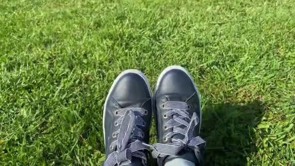 Γυναικεία πόδια σε αθλητικά παπούτσια σε ένα ηλιόλουστο πράσινο γρασίδι, κοντά. - Πλάνα, βίντεο