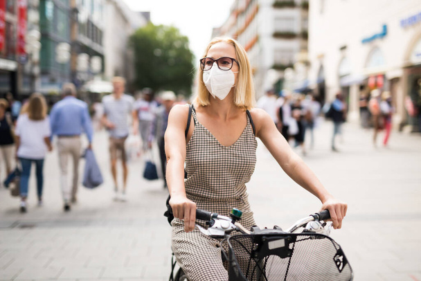 Frau, die in der Stadt Fahrrad fährt und in der Öffentlichkeit medizinische Gesichtsmasken trägt, um die Ausbreitung des Coronavirus zu verhindern. Neue Normalität bei Covid-Epidemie. - Foto, Bild
