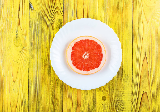 A fresh grapefruit on a white plate on a wooden background - Fotografie, Obrázek